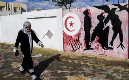 Une Tunisienne marche près d’un mur sur lequel un graffiti représente un homme en en oiseau symbolisant la liberté, le 27 octobre 2020 (AFP)