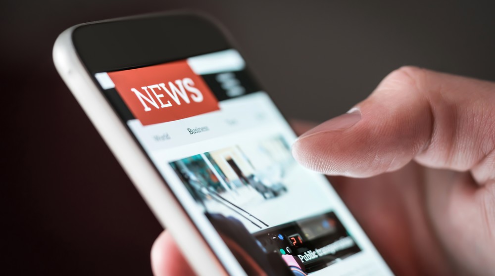 Mobile news application in smartphone. Man reading online news on website with cellphone. Person browsing latest articles on the internet. Light from phone screen.